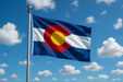 Realistic Colorado flag flying on a flagpole with blue/sunny skies behind it